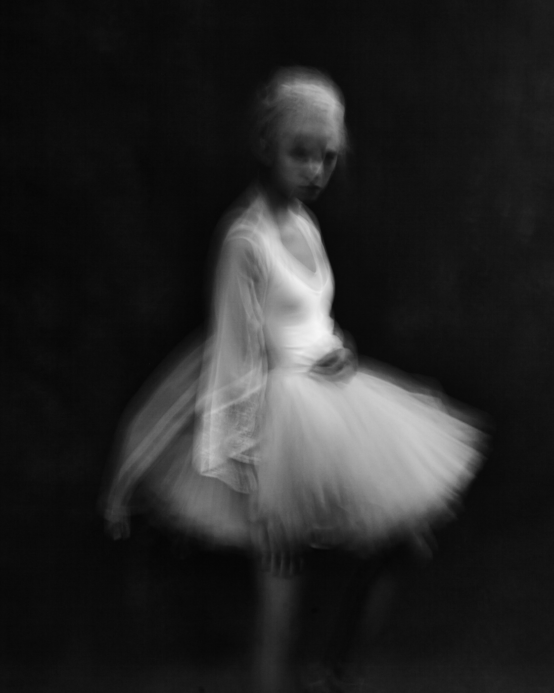 A ballerina posed in a pale tutu against a textured backdrop.