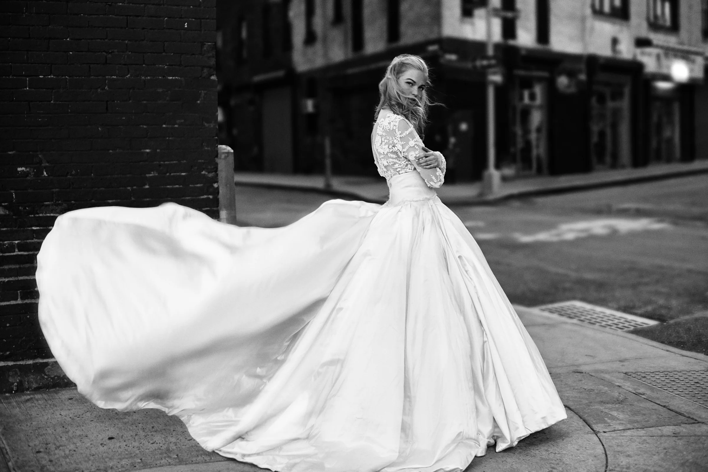 A woman turns toward the camera as a white couture gown moves across a New York corner.