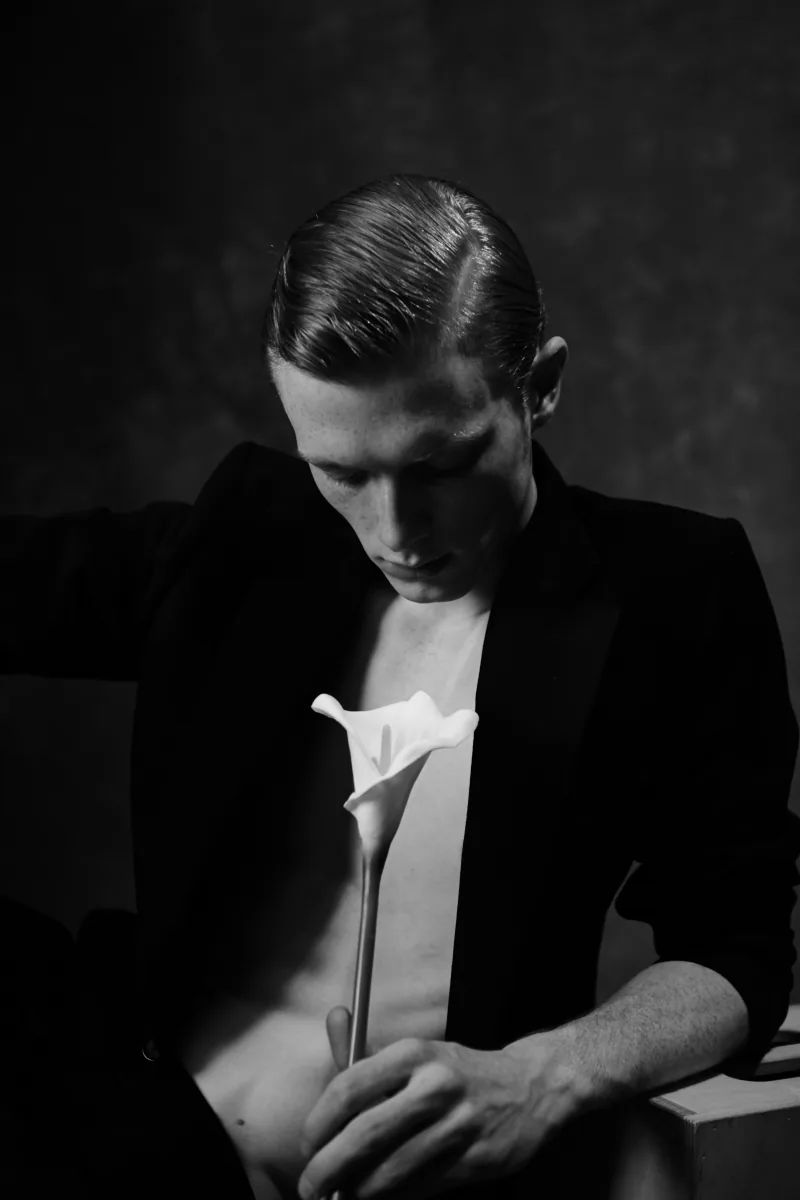 A man holds a white calla lily against a black background.